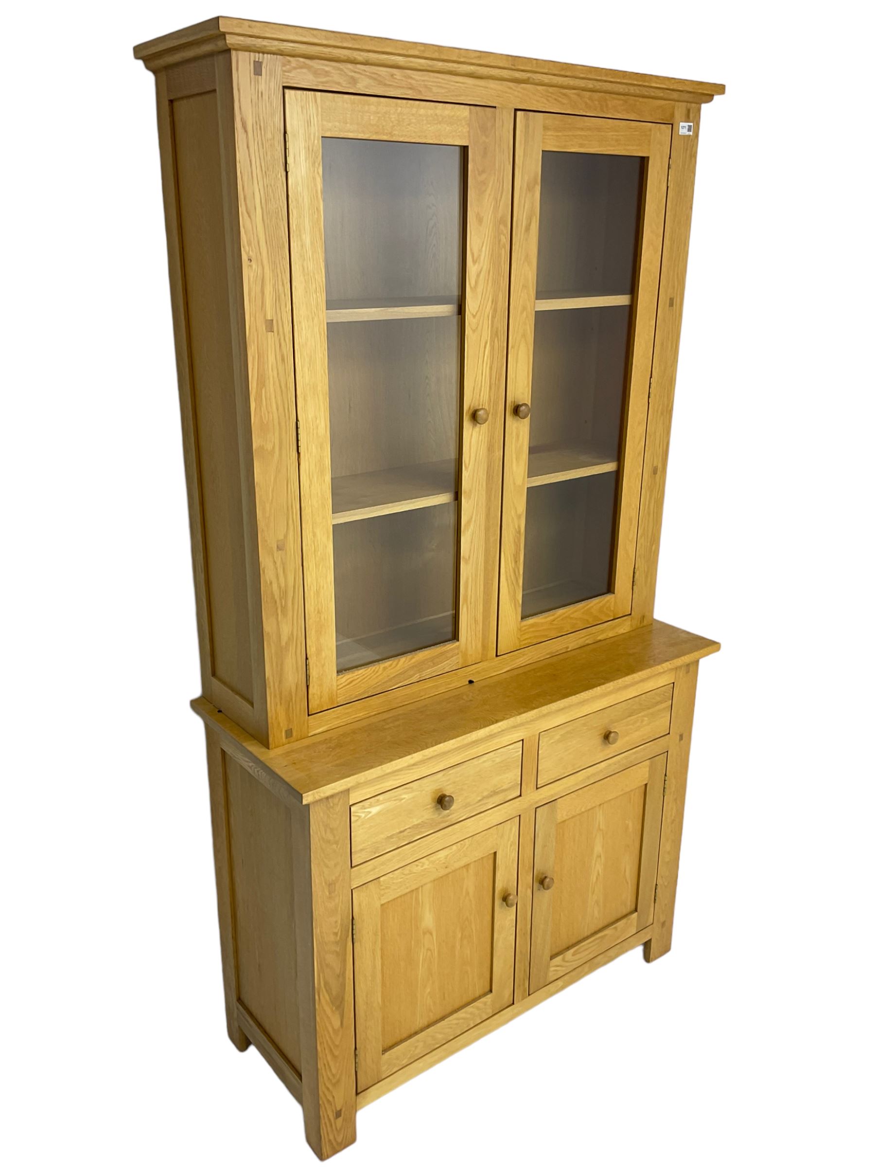 Contemporary light oak bookcase display cabinet, fitted with  two glazed doors enclosing two shelves, above two drawers and cupboards