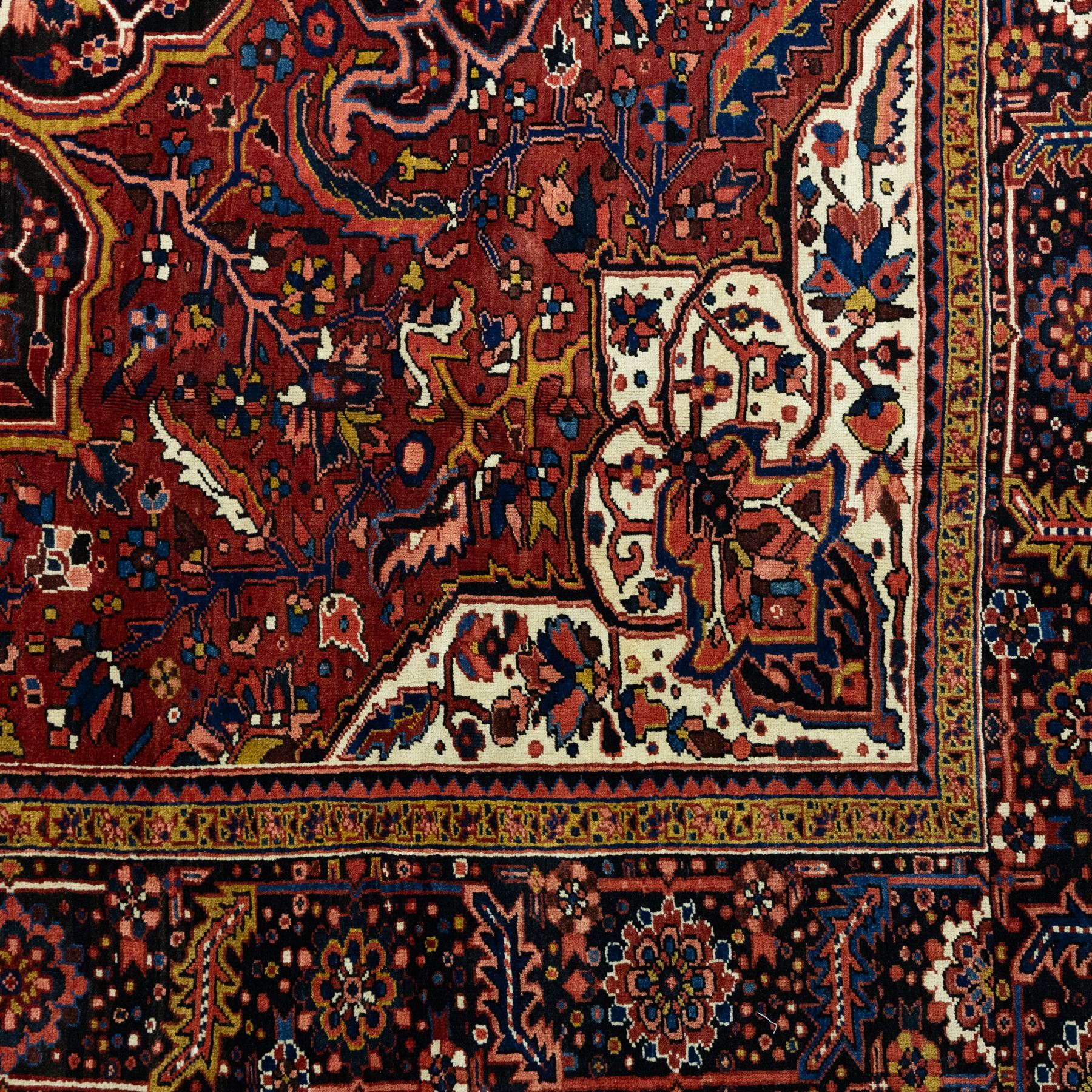 North West Persian Ahar hand-knotted carpet, madder red ground, with a large central shaped floral medallion with pendants, surrounded by angular scrolling foliate motifs incorporating rosettes, palmettes and stylised flowerheads, enclosed by ivory spandrels and a dark navy border with repeating floral motifs and meandering vines, flanked by narrow floral guard stripes, with cotton fringes