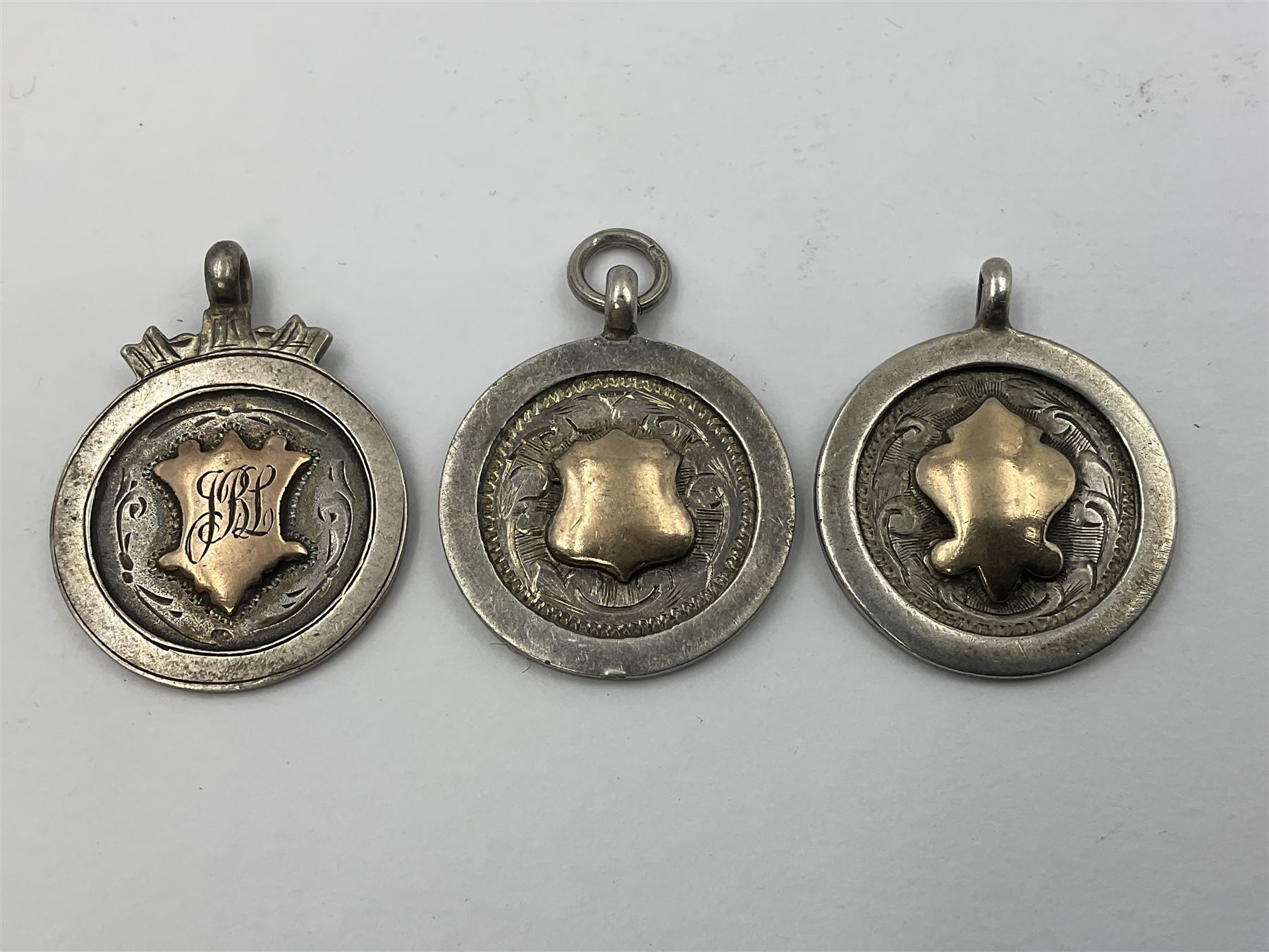 Seven early 20th century silver gold faced cartouche fobs, to include a circular example, with rose gold border and cartouche within an embossed yellow gold border, engraved verso, and a double sided example, all hallmarked with various dates and makers
