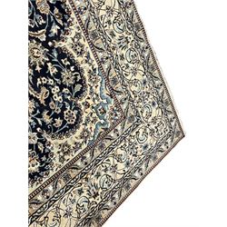 Persian Kashan indigo ground carpet, the central ivory rosette medallion surrounded by trailing and interlaced flower heads and branches, matching spandrels with floral design, the border with scrolling pattern decorated with stylised plant motifs within guards