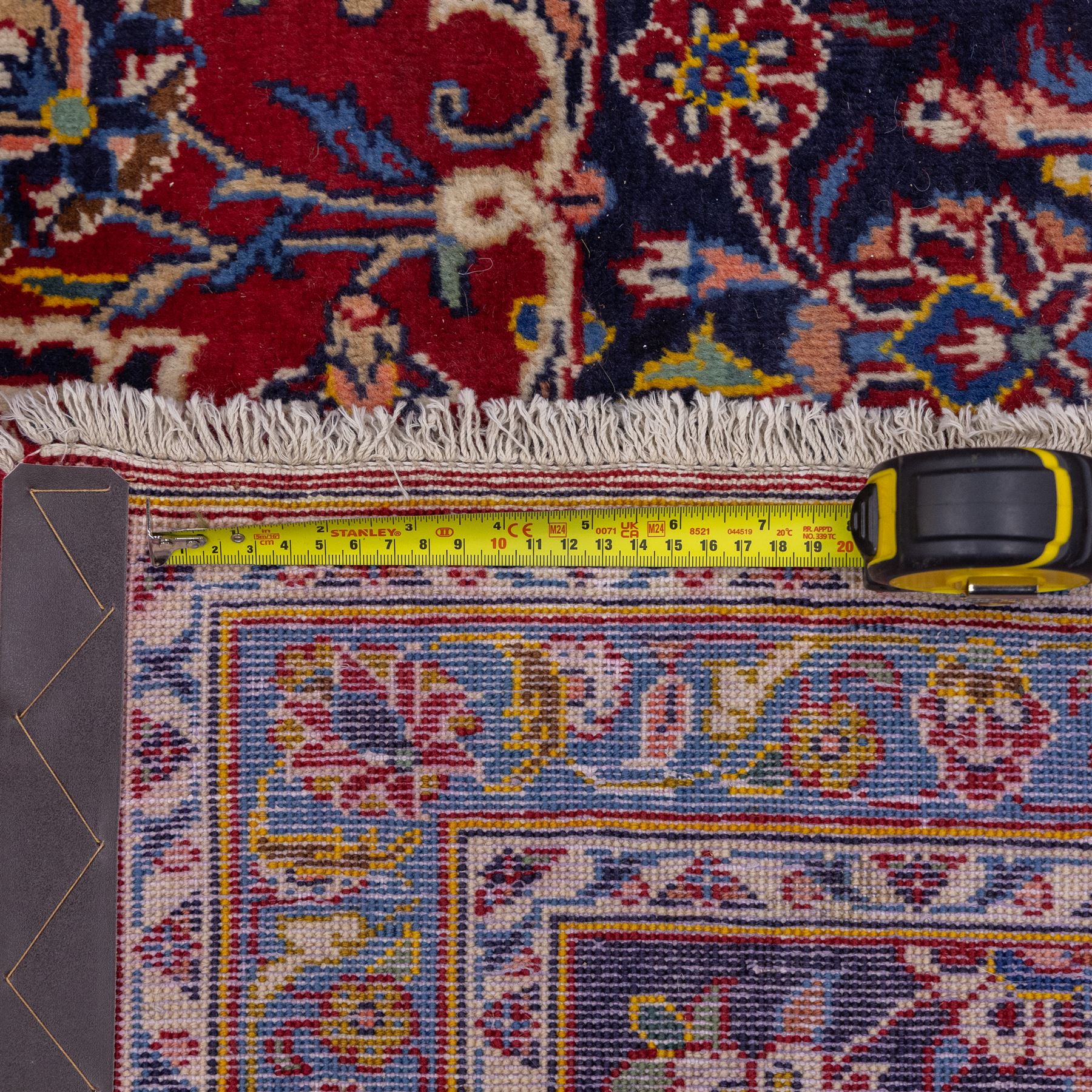 Central Persian Kashan hand-knotted carpet, madder red field with central cusped medallion in navy and ivory enclosing a floral rosette and radiating scrolling arabesques and palmettes, across a densely ornamented ground of finely drawn vinery enriched with a profusion of flowering sprays and stylized blossoms, spandrels in deep indigo and principal border of navy ground decorated with a continuous palmette and vine-scroll flanked by multiple guard stripes, with cotton fringe ends