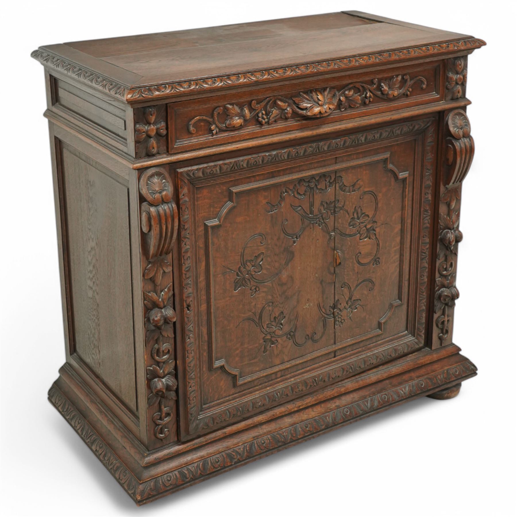 19th-century heavily carved oak baroque style cupboard with vine and floral carved frieze drawer above panelled cupboard door with floral carved appliqué (detached) flanked by symmetrically carved scroll and vine decorated sides, on bun feet 