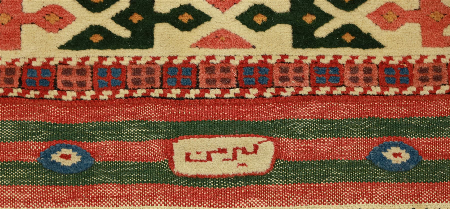 Anatolian Soumak rug, ivory ground decorated with a grid of eight octagonal medallions in terracotta red outlined in blue, centered with a star motif in vertical rows, framed by a series of geometric borders in ivory, green, and blue, incorporating hooked devices and stylized lozenges and stripped end panels, with signature at either end 