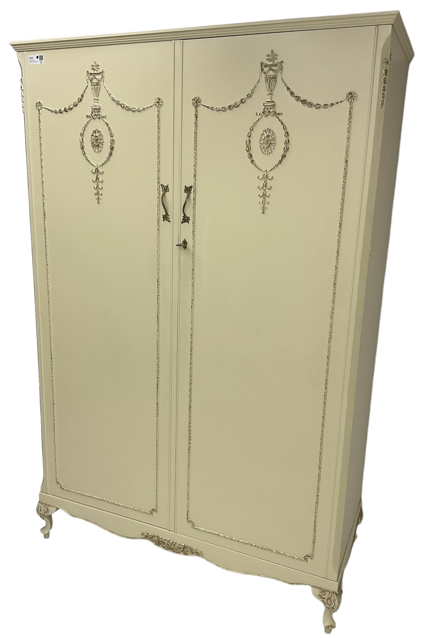 French classic design cream painted double wardrobe, the doors decorated with gilt and cream applied urn motifs with extending bell-flower festoons and ribbon twists, enclosing shelf and hanging rail, shaped apron on acanthus cabriole feet