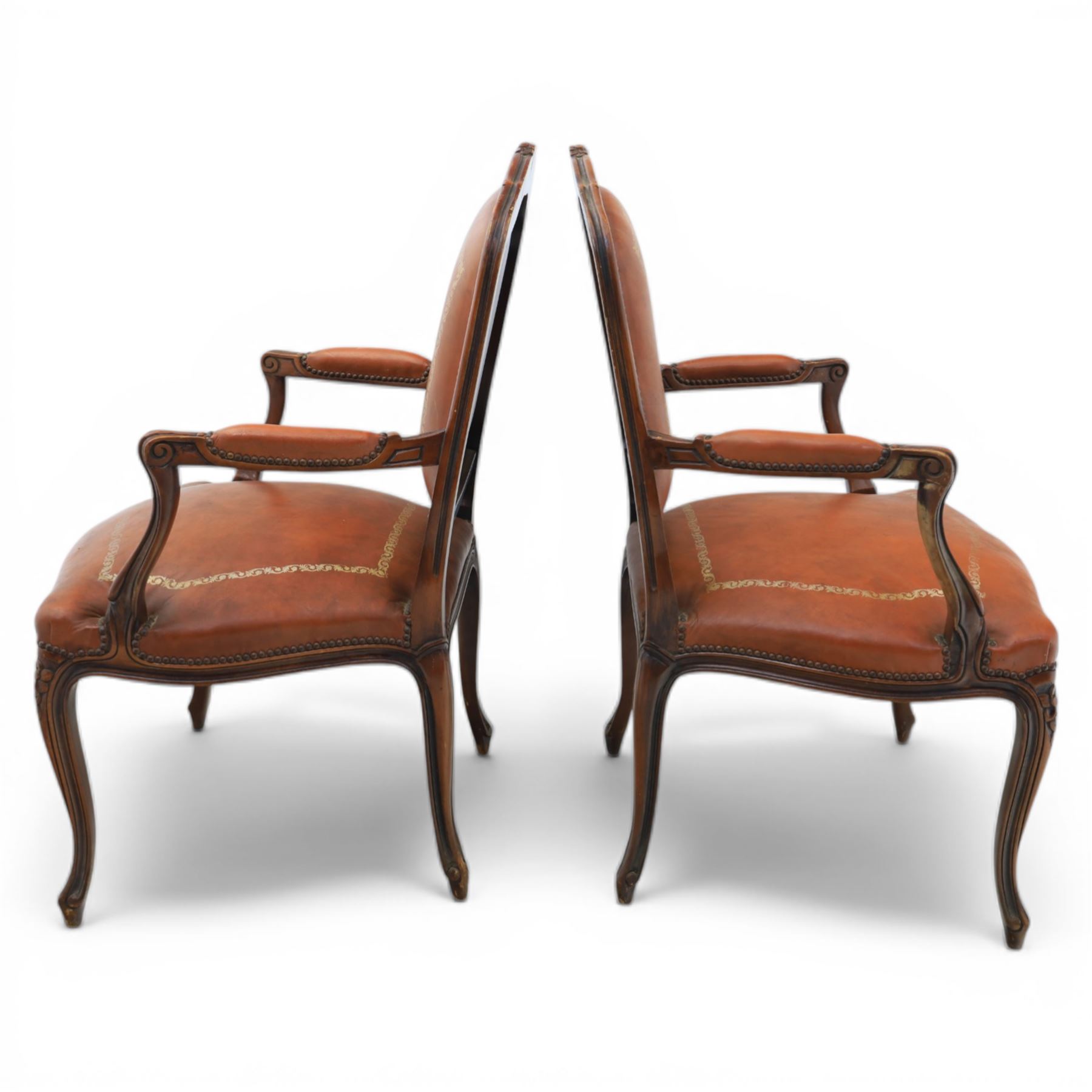 Pair of late 20th century French style carved beech open armchairs, the shaped and moulded frames with foliate cresting rail above padded backs and overstuffed seats upholstered in tan leather with gilt foliate borders and close nailed trim, raised upon cabriole supports with acanthus carved knees