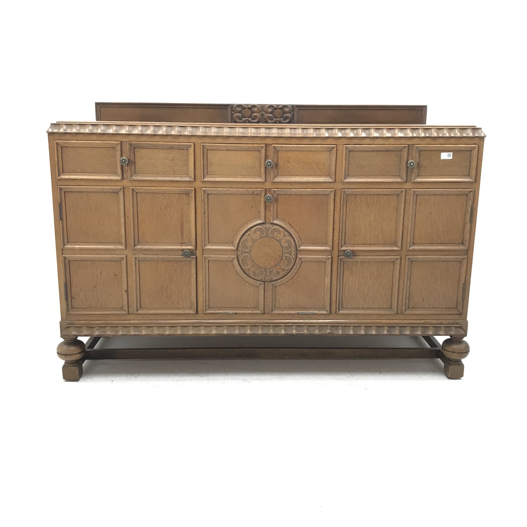 E. Gomme Ltd of High Wycombe oak sideboard, raised carved back, moulded top, three drawers above two cupboards flanking single fall front unit, turned supports joined by stretchers, W150cm, H101cm, D57cm