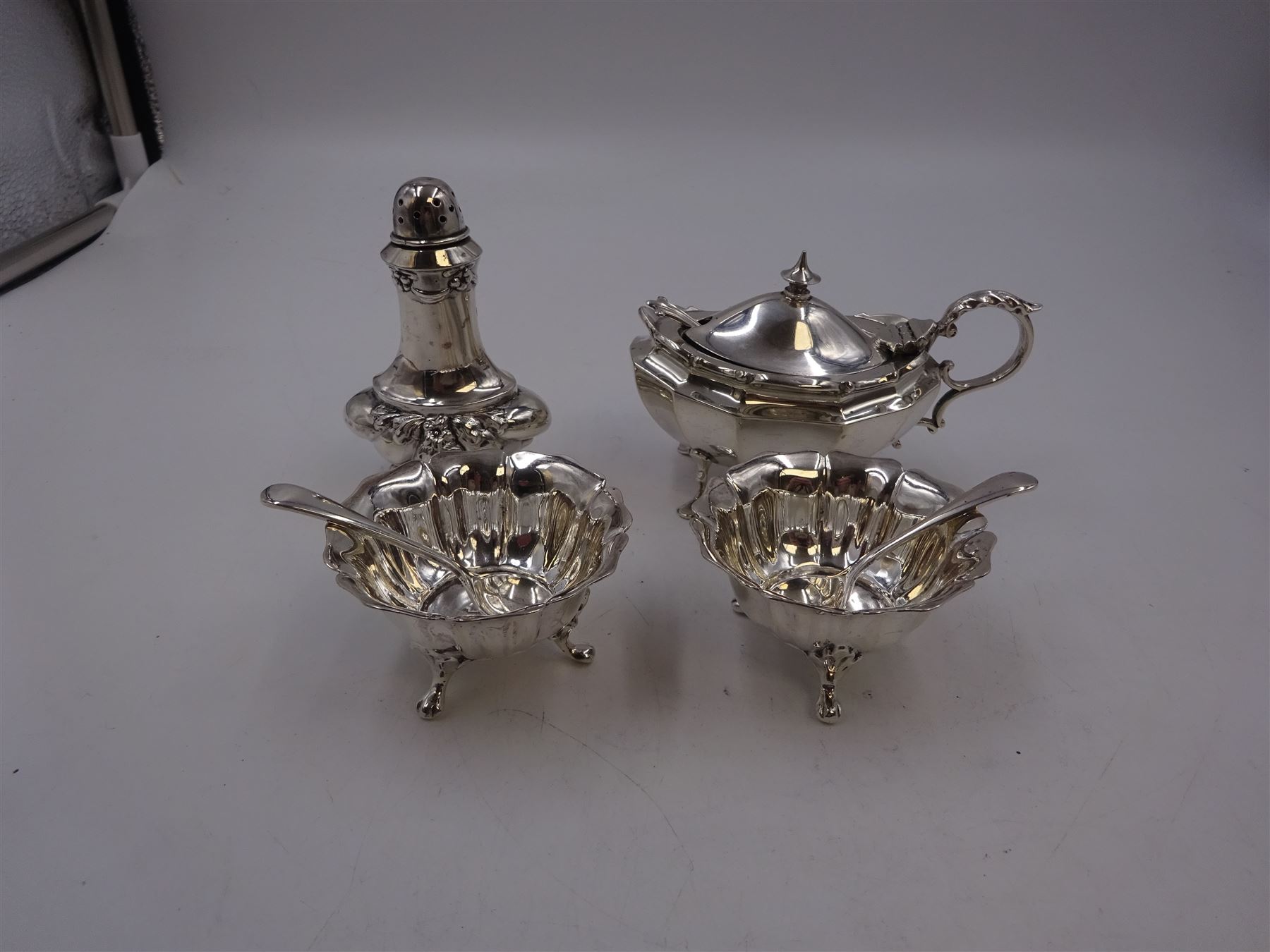 Early 20th century silver mustard pot and cover, of faceted oval form, with shaped rim and acanthus capped scroll handle, upon four pad feet, with matching spoon, H5.5cm, hallmarked I S Greenberg & Co, Birmingham 1912 & 1914, with blue glass liner, together with pair of Victorian silver open salts, of fluted circular form, with lobed rim, upon three pad feet, with matching salt spoons, all hallmarked Atkin Brothers, Sheffield 1899 and a Victorian silver pepper, of waisted baluster form, the part fluted body repousse decorated with flowers and leaves and a floral garland to upper rim, hallmarked William Oliver, Birmingham 1900