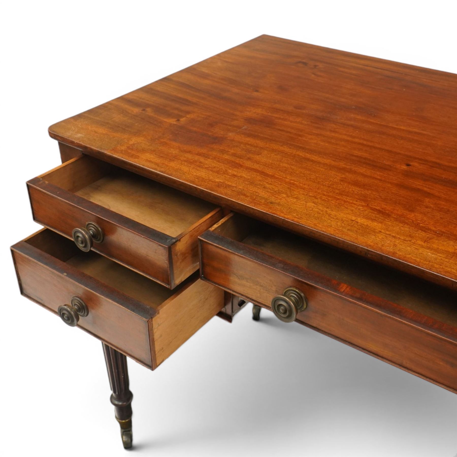 In the manner of Gillows - Regency period mahogany kneehole writing table, rectangular top over central cock-beaded frieze drawer with shaped spandrels, flanked by two graduating drawers to either side, raised on turned and fluted supports terminating to brass cups and castors