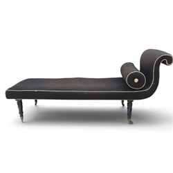 Victorian ebonised chaise longue, upholstered in black fabric with scroll headrest and bolster cushion, rectangular seat with rounded corners, raised on turned supports terminating in brass and ceramic castors
