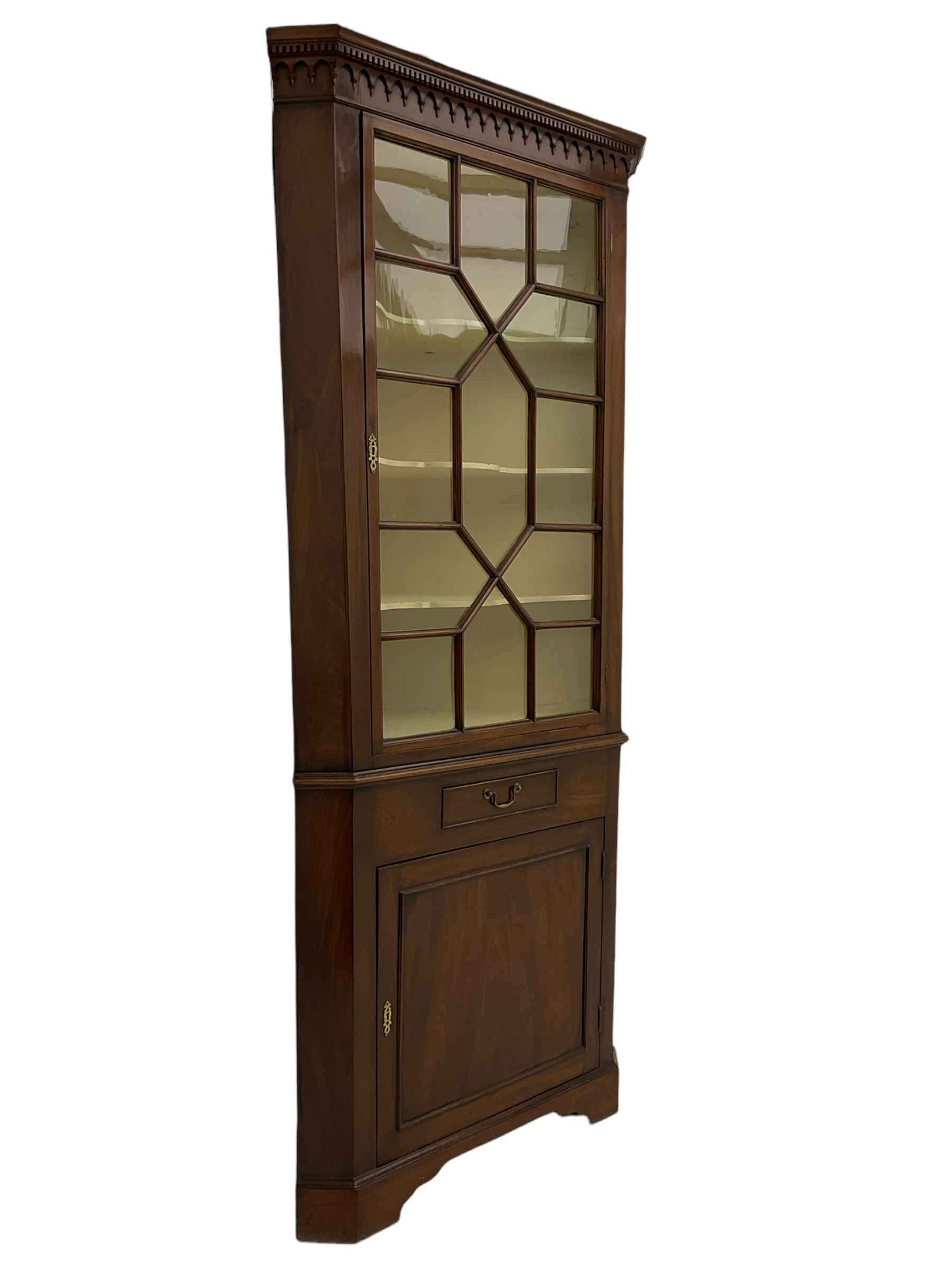 George III mahogany floor standing corner display cabinet, dentil cornice, upper astragal glazed door above small drawer and lower cupboard, on bracket feet, in two sections

