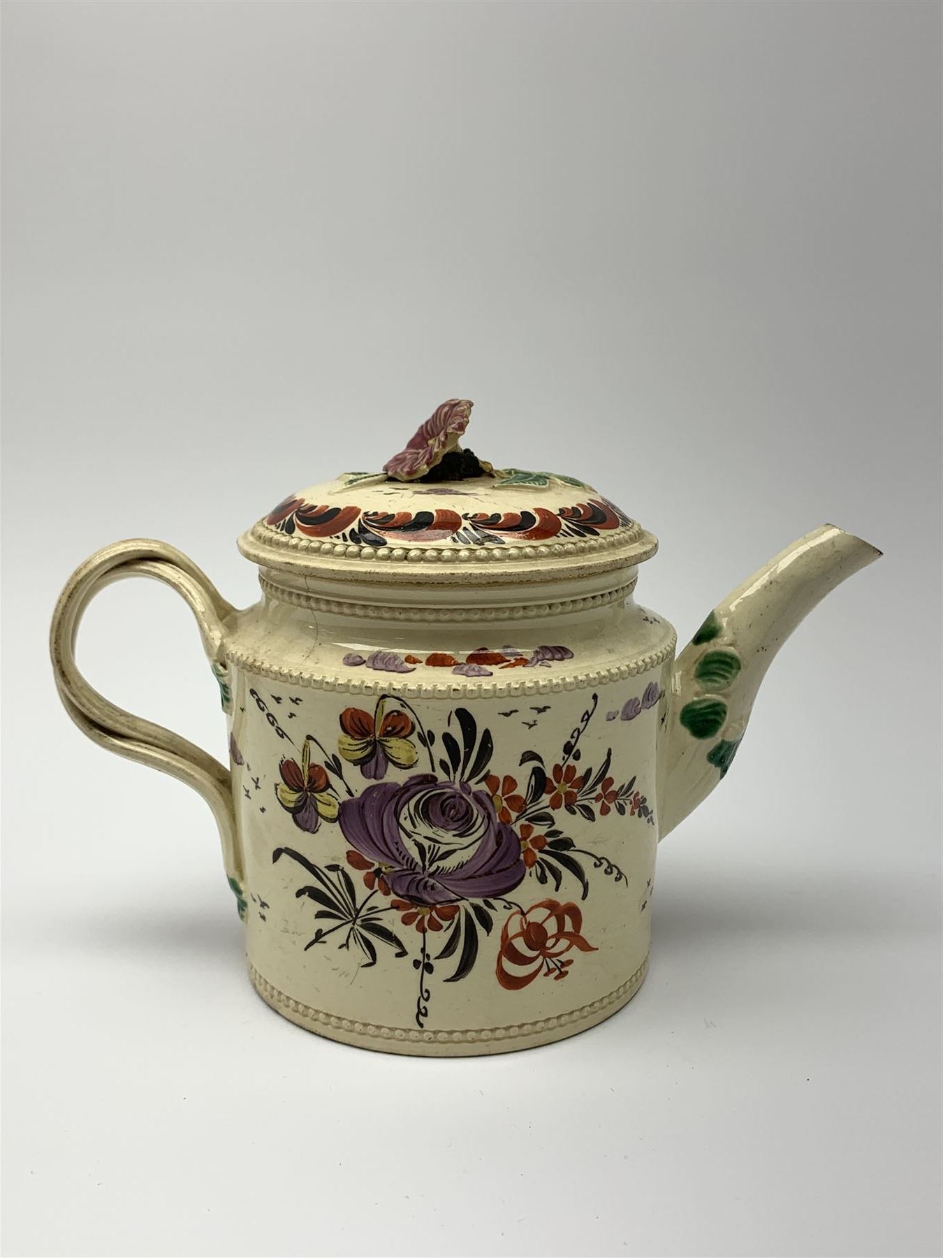 18th century creamware teapot, probably Leeds, with reeded entwined handle and floral finial to the cover, the body with hand painted polychrome decoration of figure to one side, and floral spray to the other, collectors paper label beneath inscribed Leeds Pottery, H11.5cm
