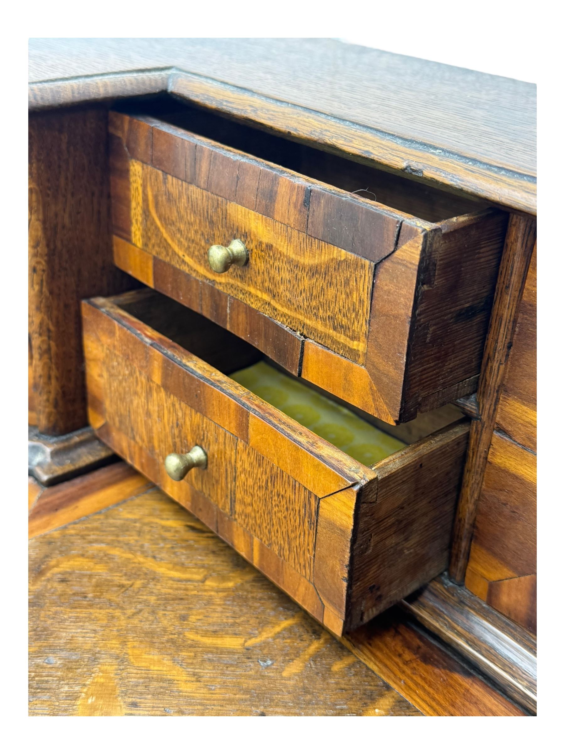 Late 19th century continental oak commode, serpentine fronted with parquetry and crossbanded decoration, the raised superstructure back fitted with a central bank of five recessed drawers flanked by concave drawers, above three full-width drawers with brass ring handles, raised on cabriole supports
