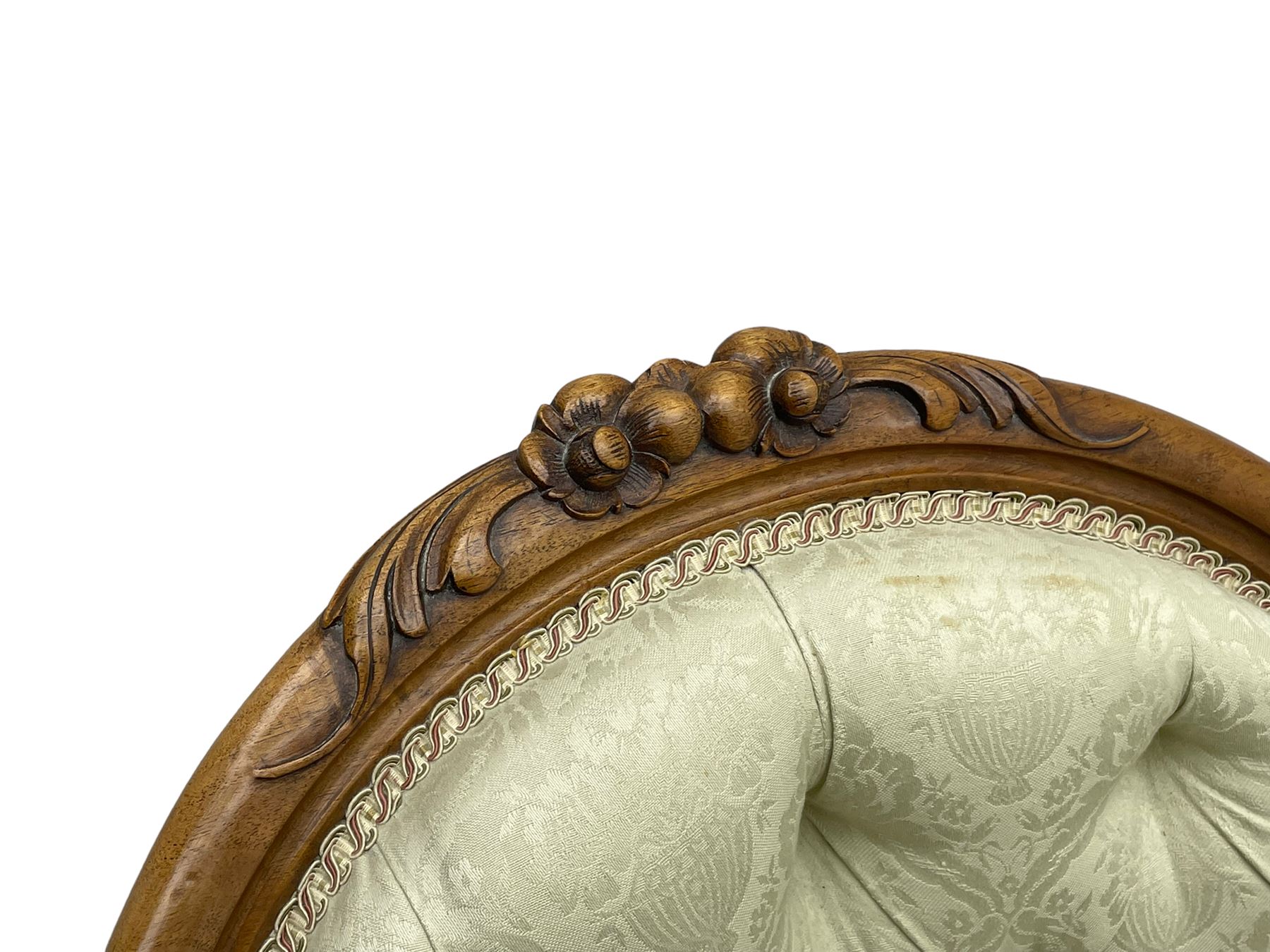 Victorian walnut framed nursing chair, the cresting rail decorated with carved applied flower heads and acanthus leaves, shaped back and sprung seat upholstered in buttoned ivory damask fabric, serpentine front over cartouche carved cabriole supports with ceramic castors (W57cm H92cm); with matched footstool, circular top over shaped moulded apron, on floral carved cabriole feet (W34cm) 