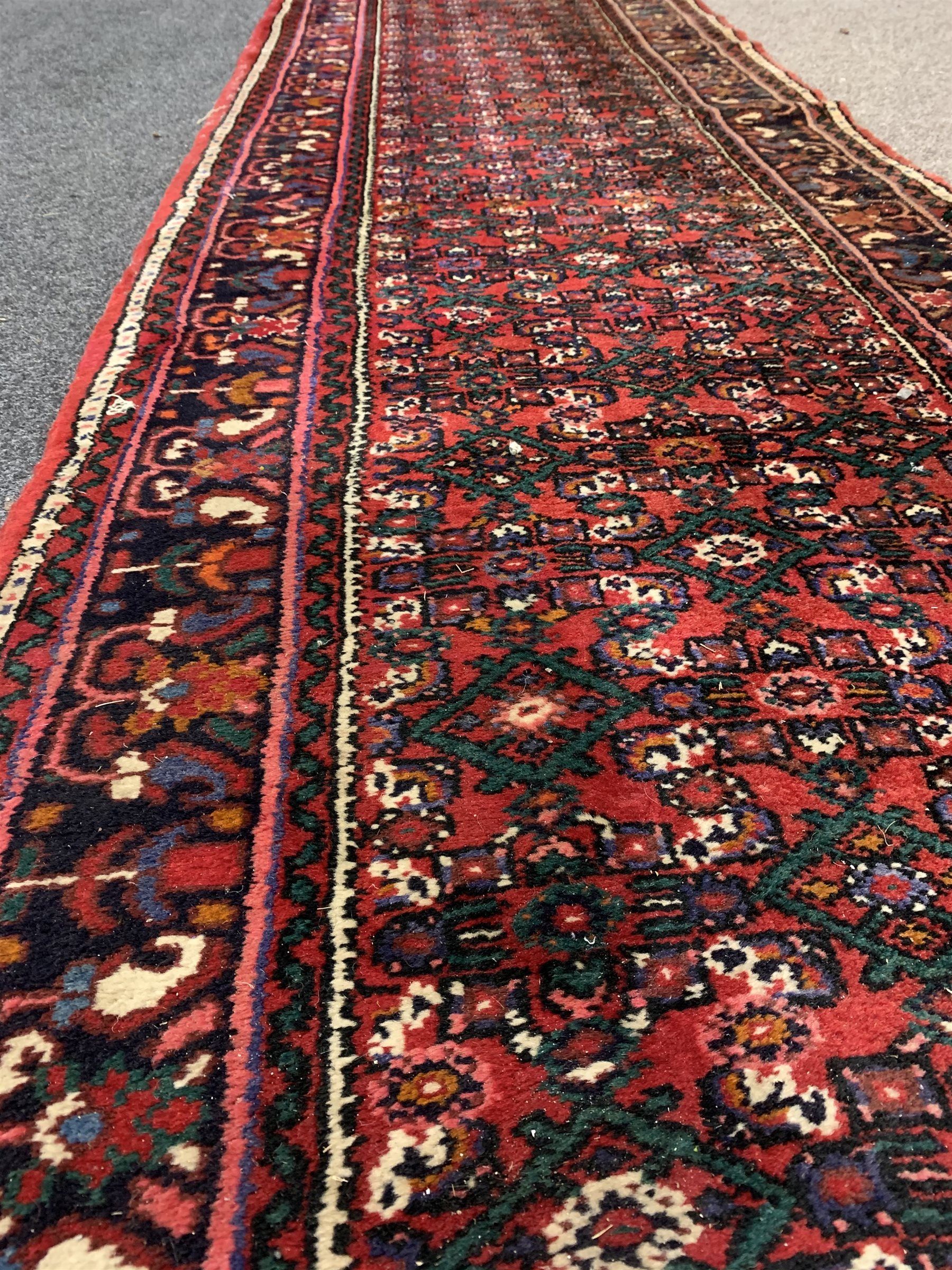 Central Asian runner rug, with repeating lozenge motif on busy red field, stylised foliate to border, 86cm x 400cm