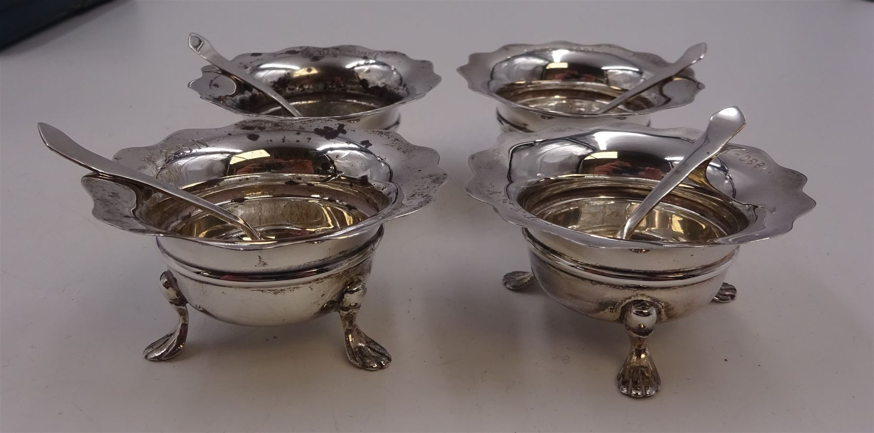 Set of four Edwardian silver open salts, of circular form, each with later personal engraving to scalloped rim and upon three pad feet, together with four matching silver salt spoons, hallmarked James Deakin & Sons, Sheffield 1909, in velvet and silk lined fitted case     