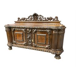 Late 19th century heavily carved walnut sideboard, raised back with pierced and carved fleur-de-lis with extending scroll and foliate decoration, moulded and carved edge with repeating cartouche design, central panel with fruit motifs flanked by two cupboards, the edge reeded cluster columns with acanthus leaf capitals, raised on large clawed feet
