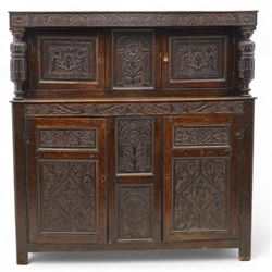 William & Mary design oak court cupboard, lunette carved frieze rail on turned and stop-fluted columns, the upper section fitted with two panelled doors carved with scrolling foliage and shield within a chip-carved border, central panel carved with arcade surrounding flower, foliate S-scroll lower frieze rail over two further cupboards and central panels, each carved with lozenges and curling foliage, moulded and pegged frame, terminating to stile supports 