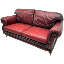 Thomas Lloyd - three-piece lounge suite, comprising of traditional shape two seat sofa (W190cm H80cm) and a pair of wingback armchairs (W100cm H91cm), each with rolled arms over turned supports with brass castors, upholstered in oxblood red leather