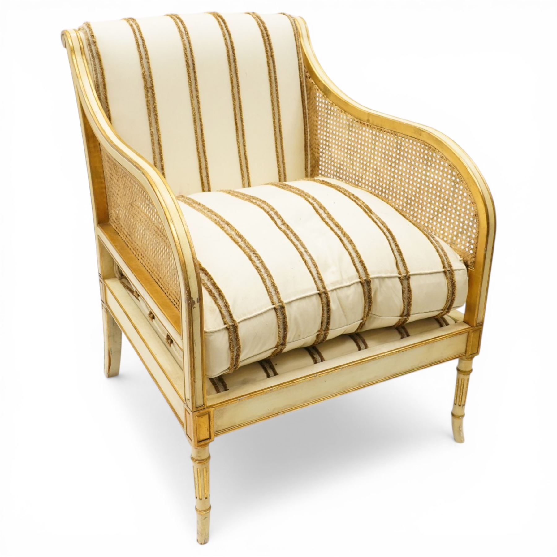 Louis XV design cream painted and parcel-gilt bergere armchair of large proportions, high scrolled back over canework arms, upholstered in striped fabric with over-stuffed loose seat cushion, on fluted supports