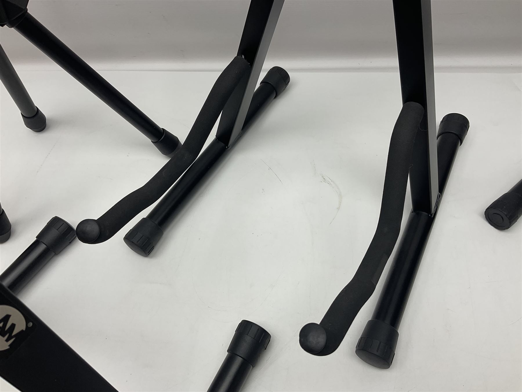 Four folding tubular guitar stands, two by RockJam; and folding tubular saxophone stand (5)