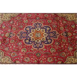 North East Persian Meshad hand-knotted carpet, crimson field with central lobed medallion in tones of indigo, ivory and soft blue, with an all-over arrangement of scrolling vinery, palmettes, and floral  sprays, conforming spandrels, main border of stylized floral vinery framed by multiple guard borders, with cotton fringe ends