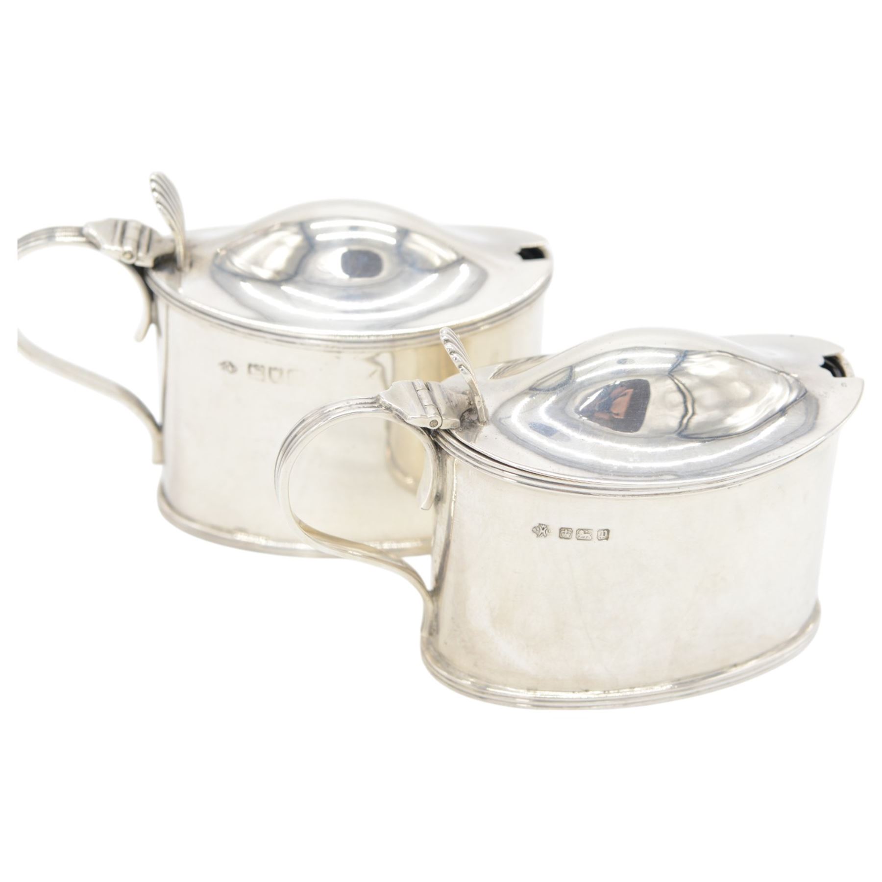 Pair of Edwardian silver mustard pots, of oval form with reed borders and palmette thumb pieces to hinged covers, opening to reveal blue glass liners, hallmarked William Hutton & Sons Ltd, London 1905, H7.5cm