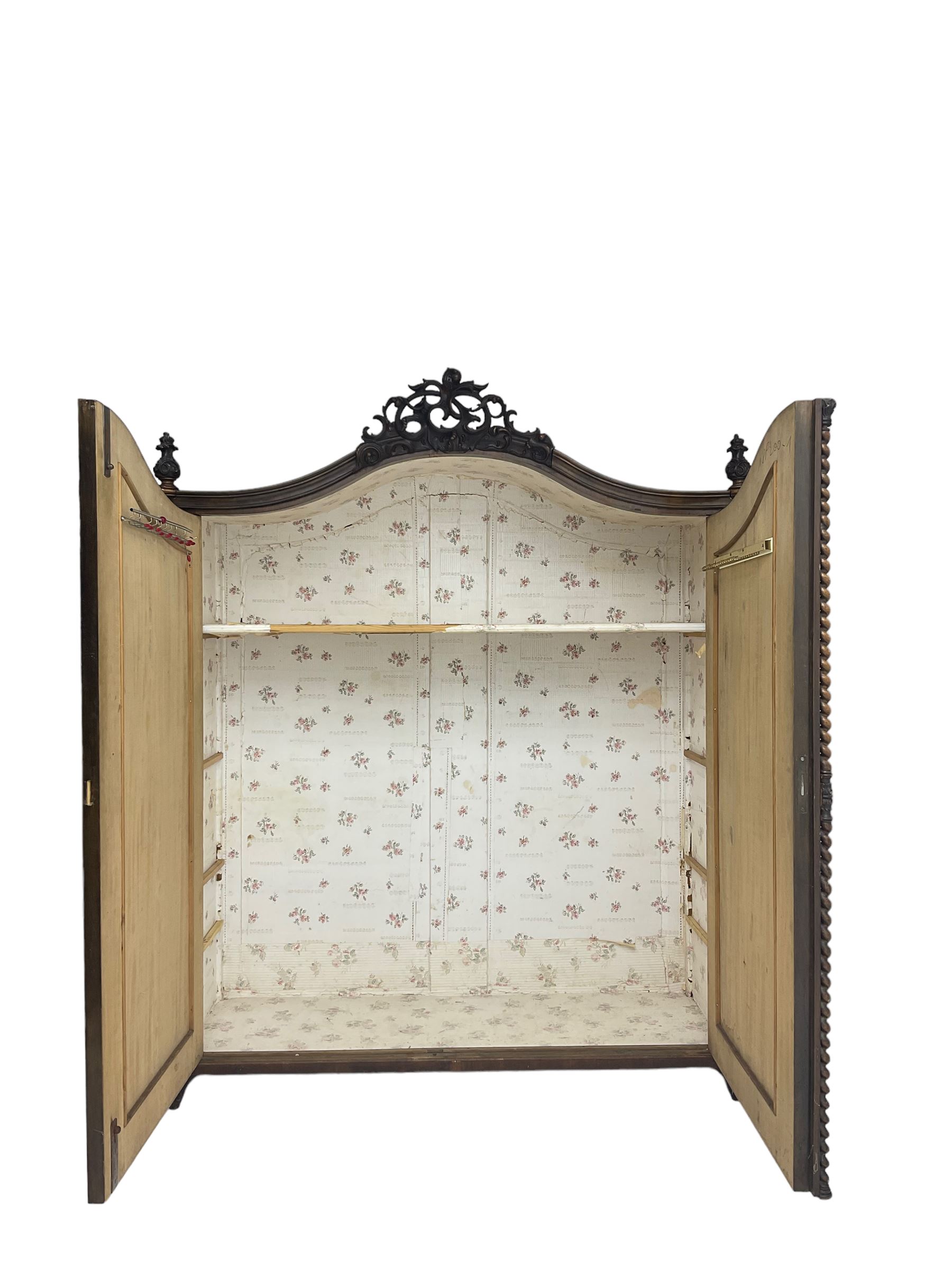 Early 20th century Italian walnut armoire wardrobe, the pierced and scrolling pediment carved with acanthus leaf detail, flanked by two scrolling cartouche with matching corbels below, the two panelled doors with applied carved rinceaux slips, with a central spiral turned upright, enclosing single shelf and hooks, raised on scroll feet