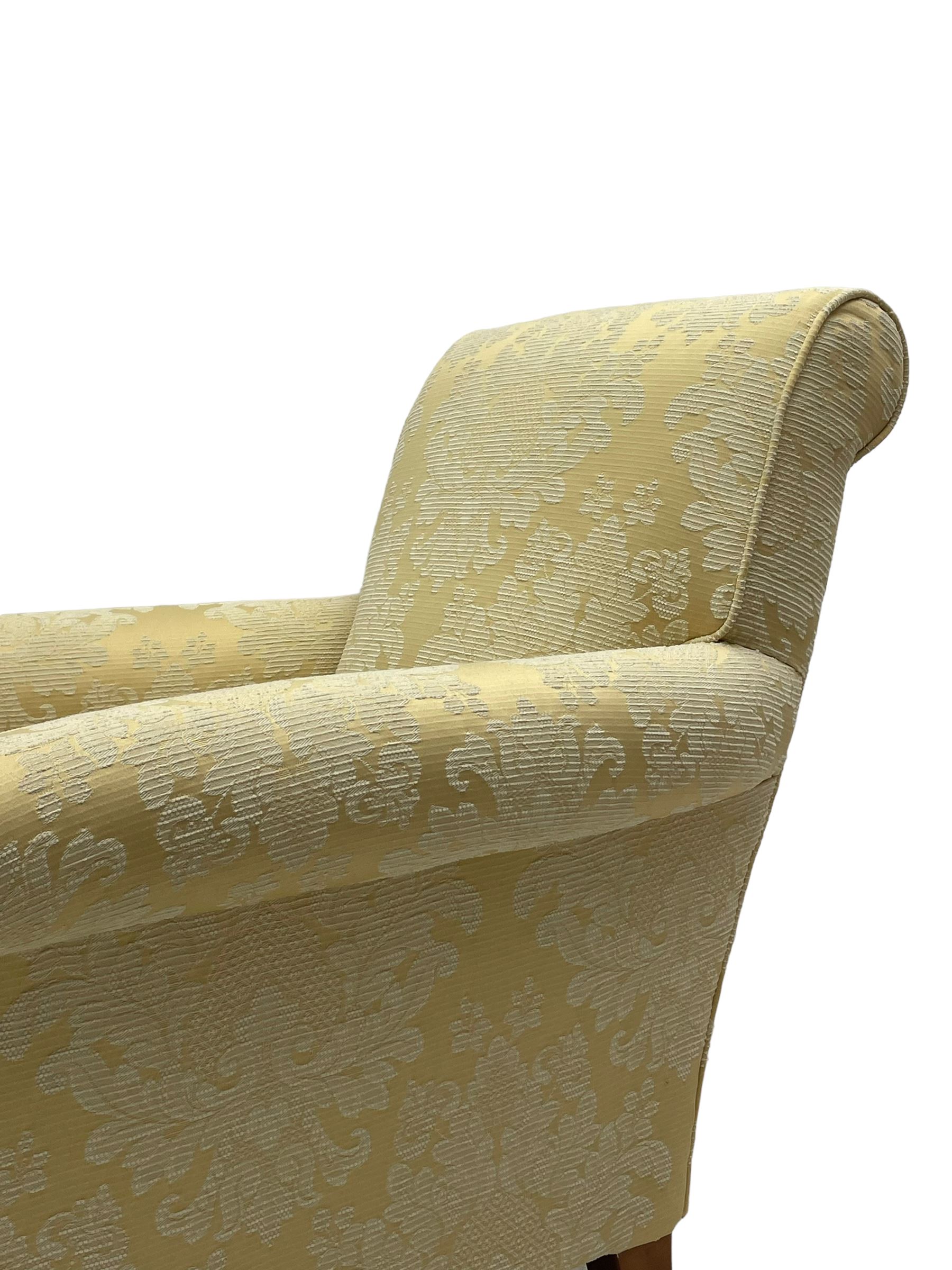 Traditionally shaped hardwood-framed armchair, rolled back and arms, upholstered in pale gold and cream damask fabric with repeating foliate pattern, on turned feet with brass cups and castors