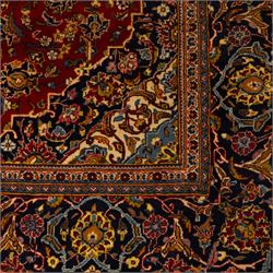 Central Persian Kashan hand-knotted carpet, crimson red field with a central shaped palmette medallion with pendants, filled with dense scrolling and floral motifs, enclosed by a navy blue border decorated with palmettes and meandering vine scrolls, flanked by multiple guard stripes, with cotton fringe ends 