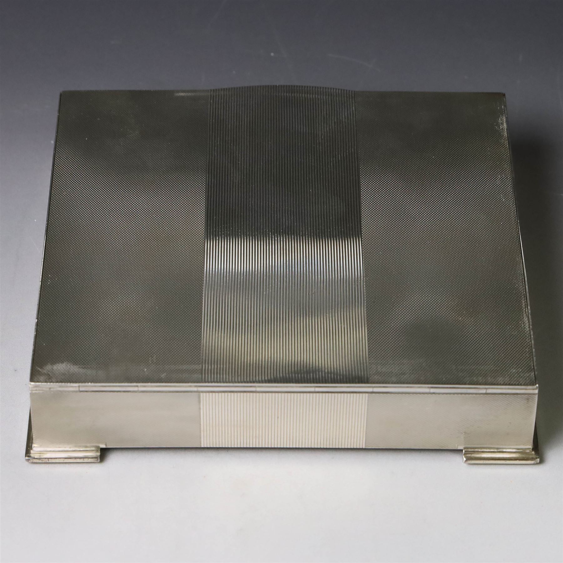 1960s silver mounted cigarette box, of rectangular form with engine turned decoration, upon four bracket feet, with presentation engraving to interior lid reading  'British Aircraft Corporation (Operating) Limited Commemorating the Queen's Award to Industry 1967, hallmarked James Geraghty, Birmingham 1965, with retailers mark for Asprey, W16.5cm, H4.5cm, in Garrard & Co Jewellers box