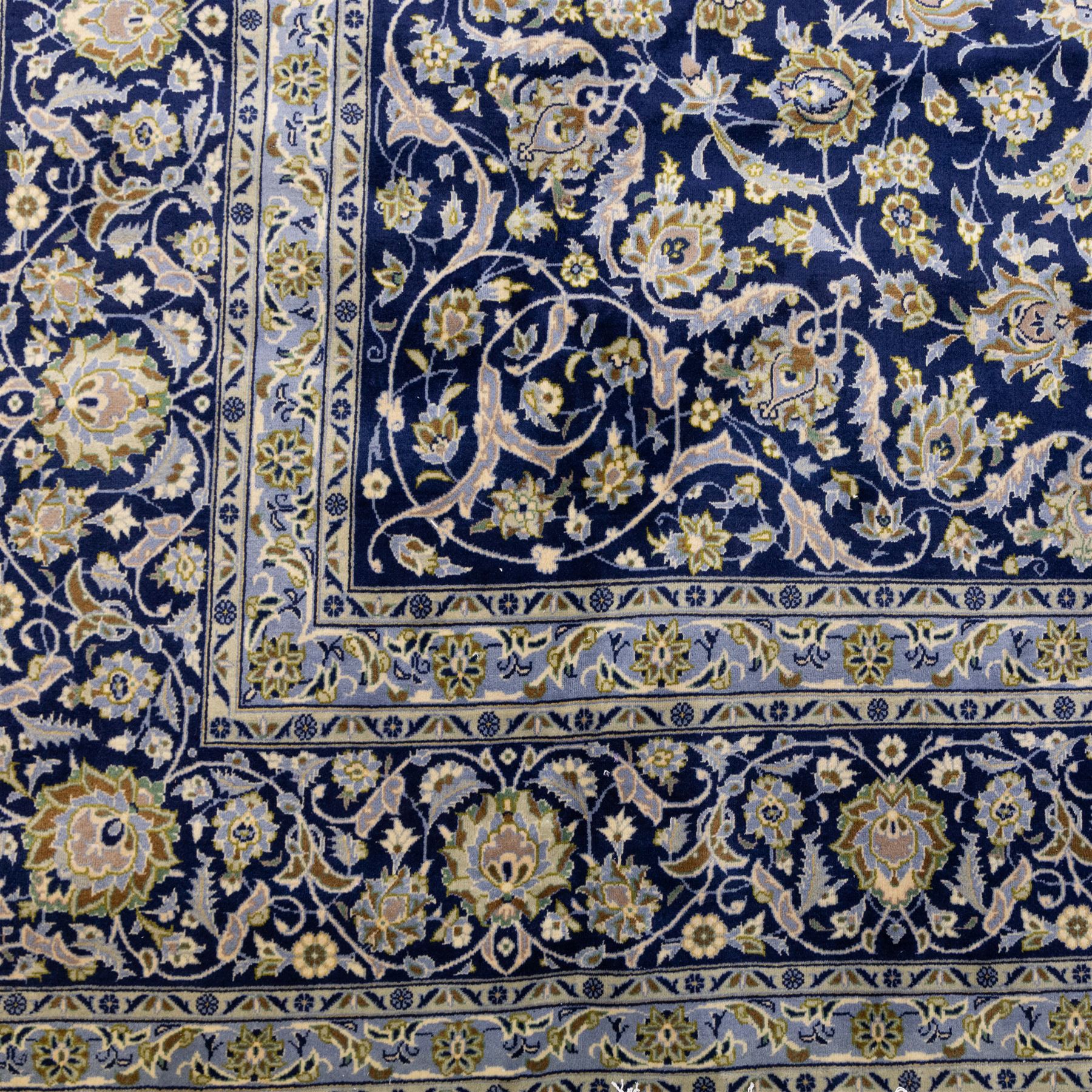 Central Persian Kashan hand-knotted rug, deep blue all-over field, finely decorated with dense scrolling floral sprays, palmettes, and flowering vines in ivory, soft gold, and pale green tones, enclosed by a multi-band floral border with corresponding guard stripes, with cotton fringe ends, signed Shah Abassi Workshop 