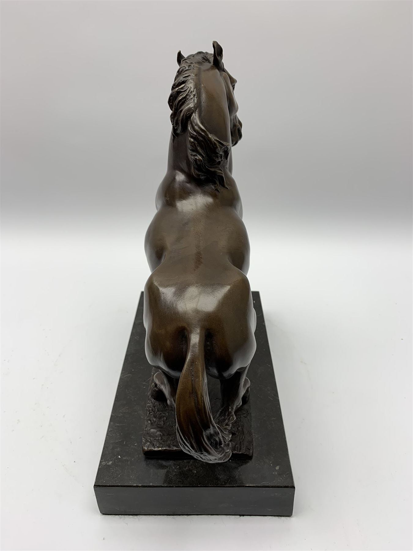 Bronze figure modelled as a prancing horse, upon a naturalistically modelled rectangular base, and black marble plinth, H34.5cm, L31cm
