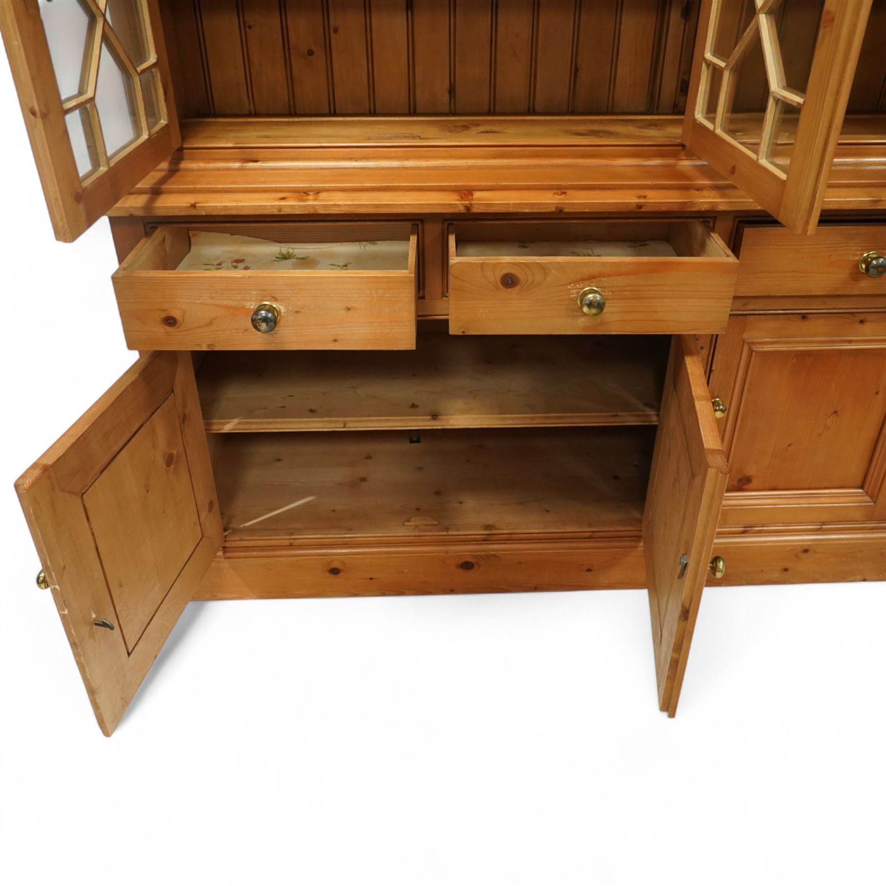 Mid 20th century pine glazed dresser on cupboard base, upper section of rectangular form with three astragal glazed hinged doors enclosing two adjustable wooden shelves and projecting frieze over three short drawers and three hinged panelled cupboard doors with brass handles, the front and sides, raised on a plinth base 