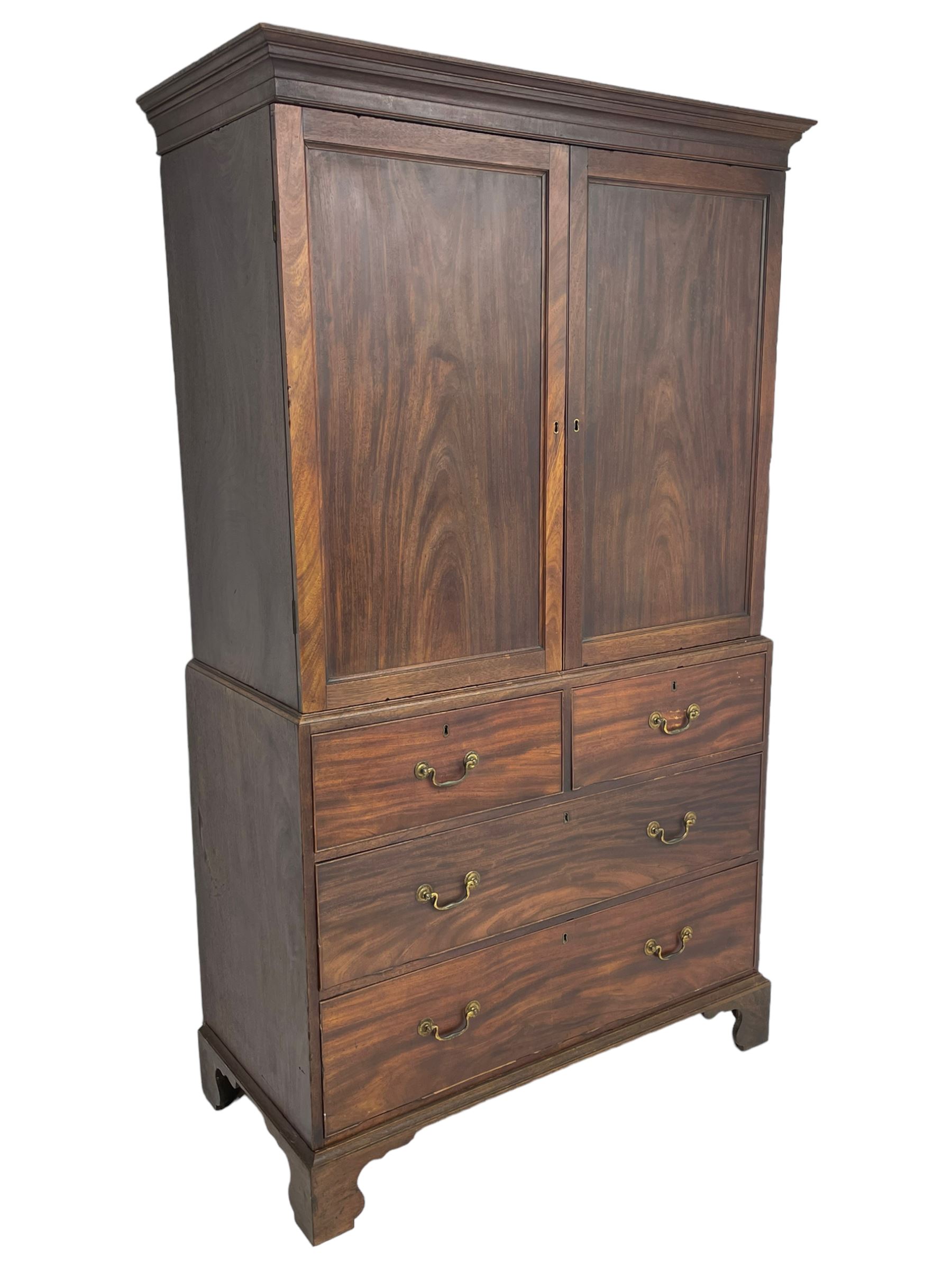 George III mahogany Gentleman's linen press, the projecting cornice over two panelled cupboard doors enclosing three sliding trays, the base fitted with two short over three long graduating cock-beaded drawers, lower moulded edge over bracket feet