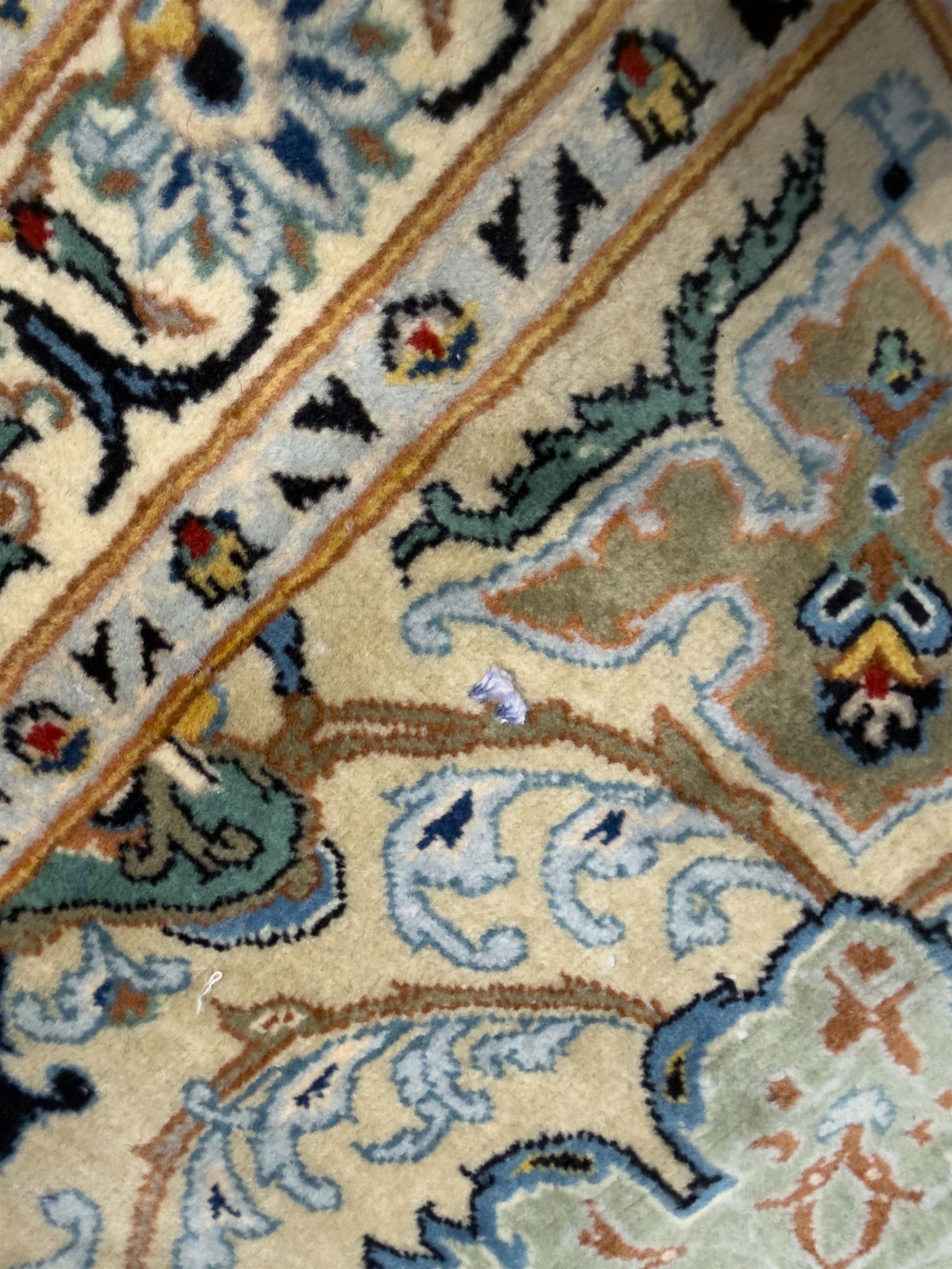 Central Persian Kashan hand-knotted carpet, ivory field with scrolling vines, palmettes, and rosettes around a cusped medallion with pendants and spandrels within a blue ground border of palmettes and flowerheads, 388cm x 300cm