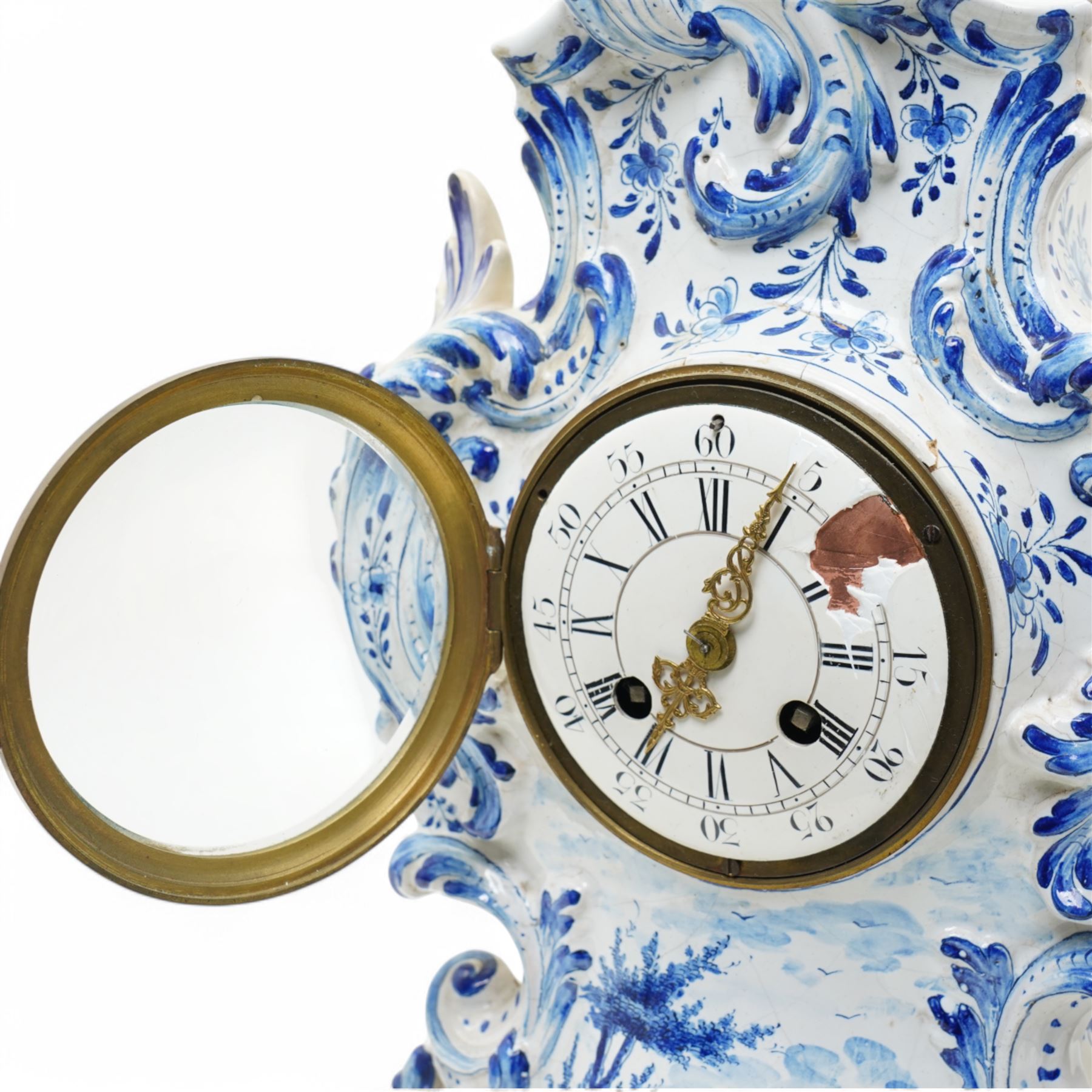 19th century delft blue and white Rococo style 8-day mantle clock, with a scrolling case and floral decoration, depiction of a courting couple in 18th century dress to the front and a contrasting scene of sailing ships on a lake to the rear, with a late 19th-century French twin train movement, enamel dial with Roman numerals, five minute Arabic's and gilt Louis XVI hands within a glazed cast bezel, with a rack striking movement sounding the hours and half-hours on a bell. No pendulum or key.  