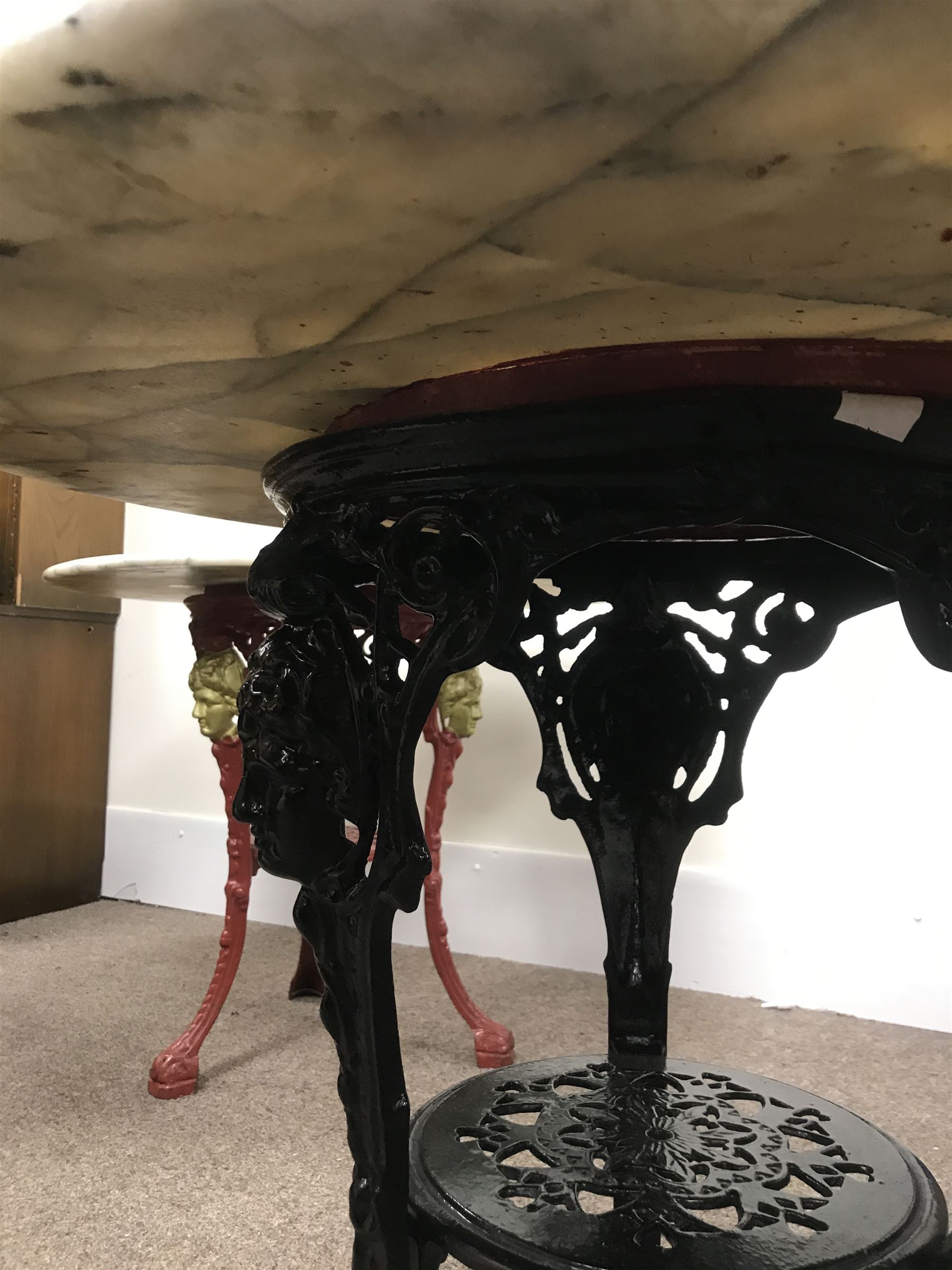 Pair cast iron Britannia pub tables, one red, one black with large marble tops 