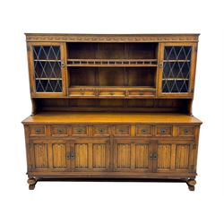 Large mid-20th-century oak dresser with two astragal glazed doors between gallery shelf and lower shelf, with three short drawers and lower section with four drawers and three double-panelled linen-fold hinged cupboard doors 