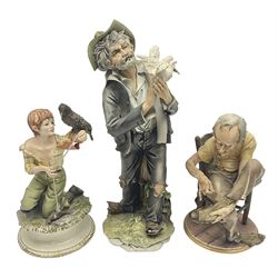 Three Capodimonte figures, to include The Kind Heart Man, modelled by Cortese as a tramp with two doves, The Young Falconer by Maria Angela and another modelled as a tramp darning his socks, all with printed marks, tallest H39cm