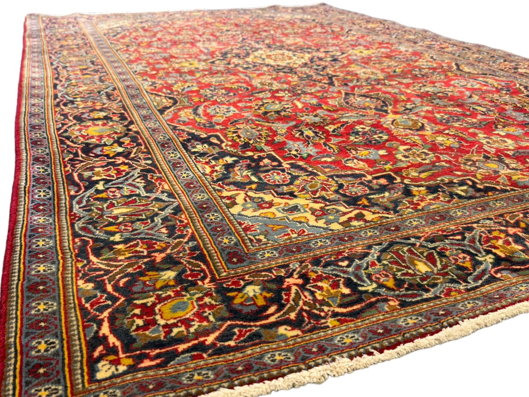 Central Persian Kashan crimson ground rug, central indigo pole medallion surrounded by sparsely placed bouquets interconnected with foliate branches, the guarded border with repeating palmette and Boteh motifs with interwoven scrolling patterns, framed by guard stripes