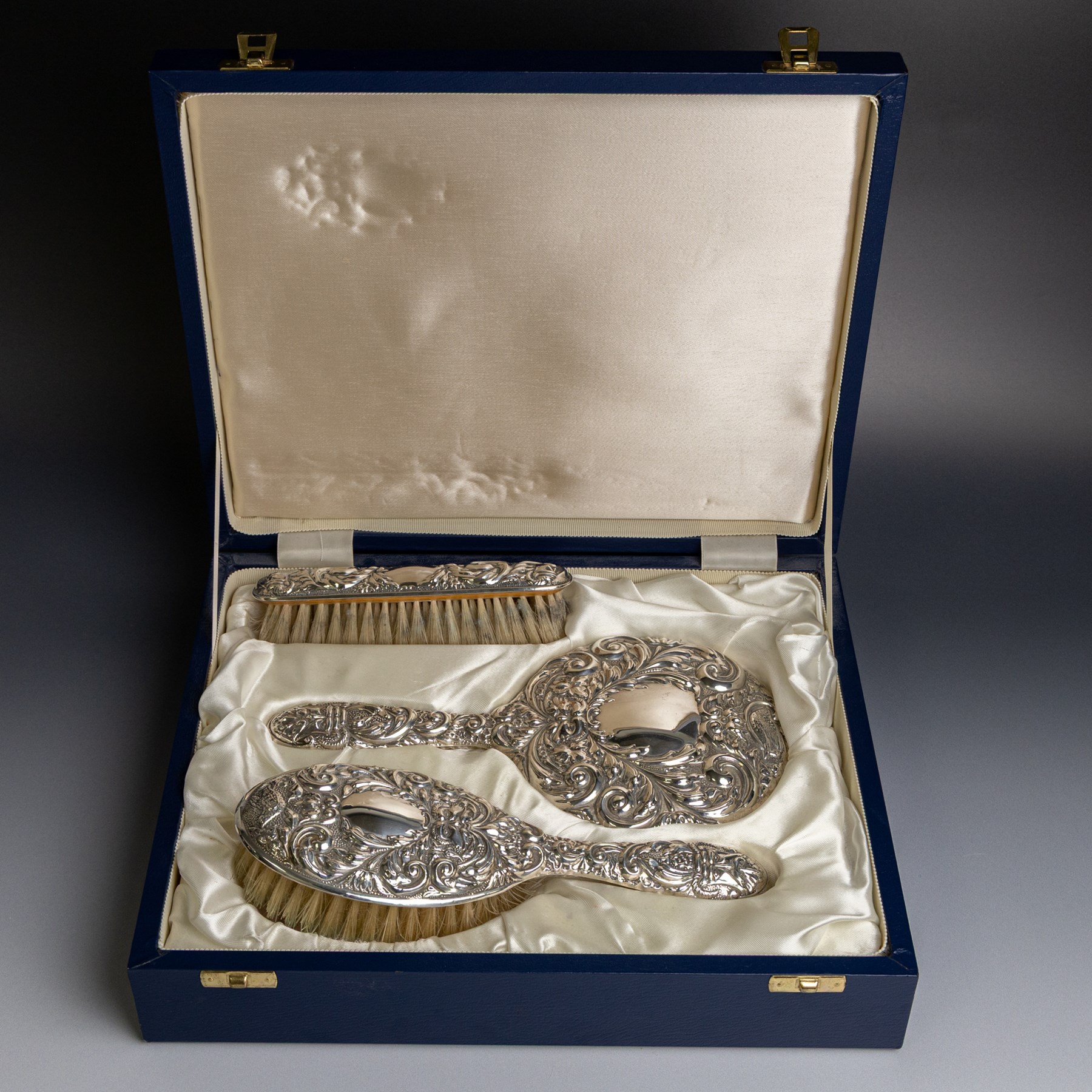 Silver mounted three piece dressing table set, comprising hand mirror, hairbrush and clothes brush, all with embossed green man and floral decoration, stamped Filled and hallmarked Broadway & Co, Birmingham 2001, contained within presentation box