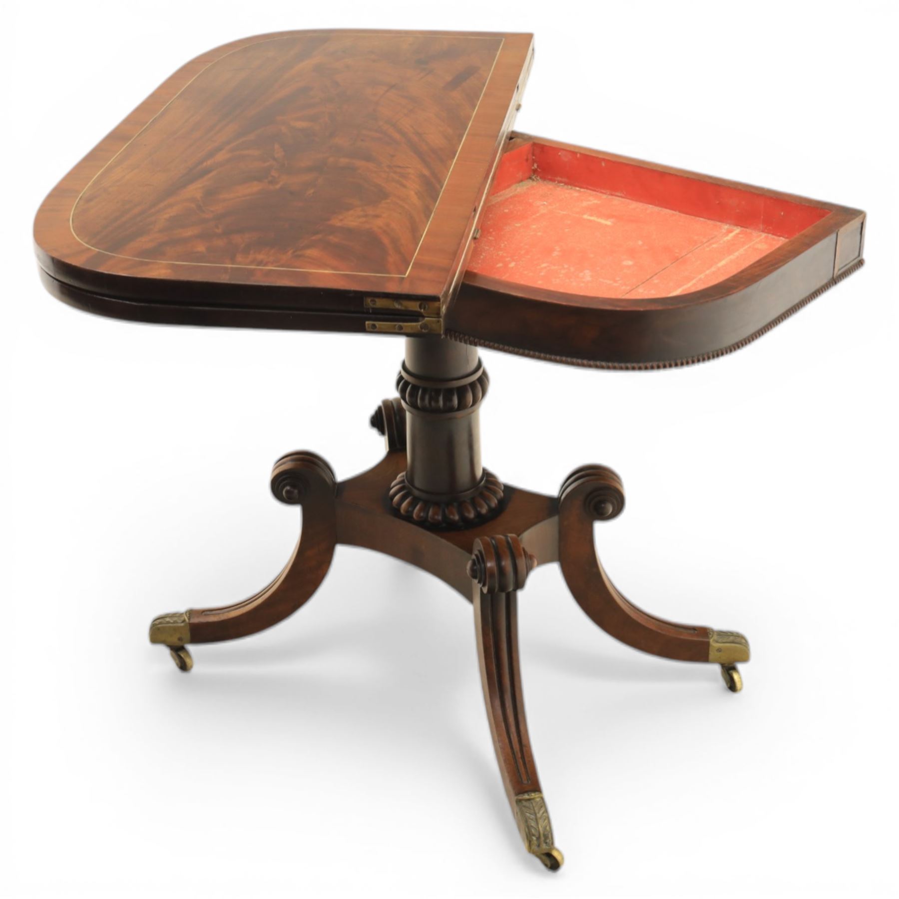 Early 19th century Regency mahogany fold over card table, the rounded rectangular top with brass line inlay enclosing green baize playing surface, crossbanded and strung exterior, with reeded edge above a gadrooned frieze, raised upon a turned column and four reeded sabre supports terminating in brass caps and castors