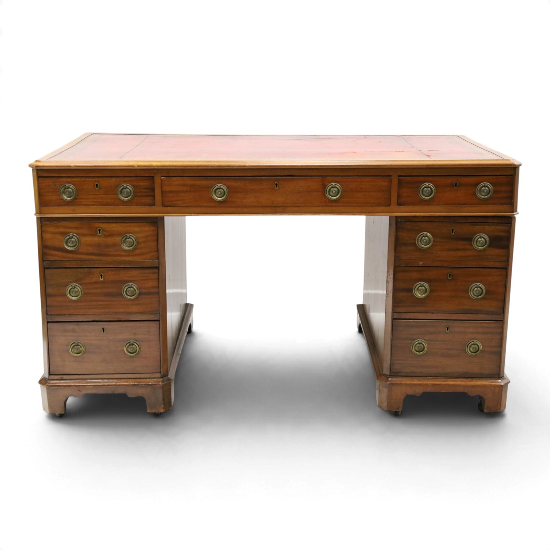 Late Victorian mahogany desk with red leather top, rectangular top with inset toold red leather writing surface, central long frieze drawer flanked by two short drawers, above pedestal with three graduating drawers with ring pull handles, on moulded plinth bases raised on castors