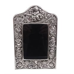 Modern Britannia standard silver mounted photograph frame, of rectangular form with arched top, heavily embossed with figural, palmette, scroll and foliate decoration, with wooden easel style support verso, hallmarked Paul Vernon Fitchie, London 2006, H23.5cm, W15cm