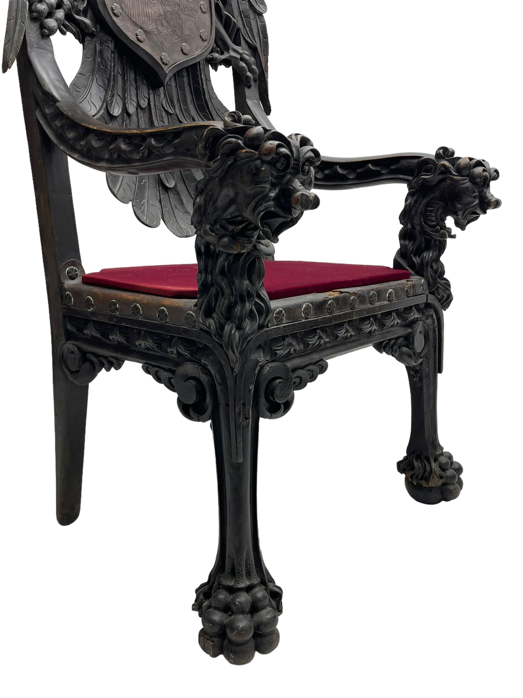 Grand mid-to-late 19th century heavily carved beech framed throne chair, the crown pediment carved with flower heads and cross finial, scroll and acanthus carved upright supports with twin perching griffin back enclosing etched leather work heraldic shield with castle and lion motifs over splayed feathers, flower head carved down sweeping arms with grotesque carved terminals, the seat rails carved with further flower heads on moulded supports with oversized ball and claw carved feet

Provenance: A very similar chair was used in the filming of Stanley Kubrick's 'Eyes Wide Shut' (1999)
