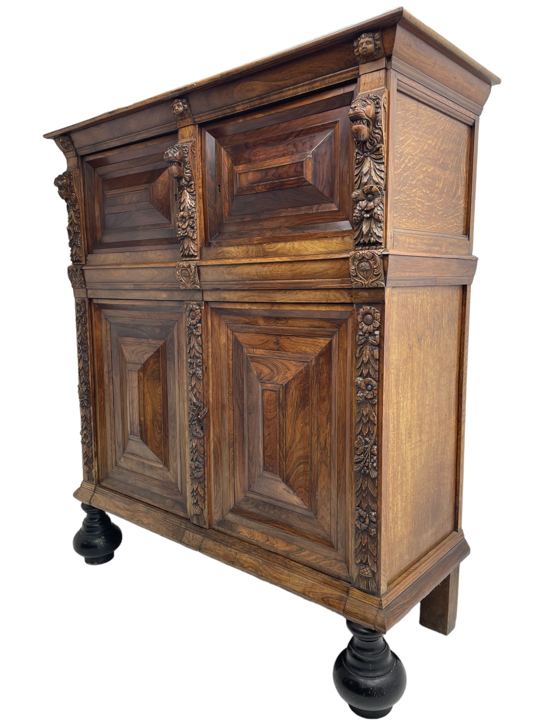 Late 17th century Flemish/Dutch rosewood and oak ‘Zeeuwse Kast’ or cupboard, projecting cornice carved with three putti masks, the uprights carved with lion masks over ribbons, flower heads and foliage, enclosed by four geometric panelled doors, lower central upright carved with flower head over foliate ribbon with bird among foliage, the escutcheon hidden by swivel berry carved cover, interior fitted with shelves, two drawers and shallow hinged cupboard, on two large turned and ebonised feet, circa 1680
