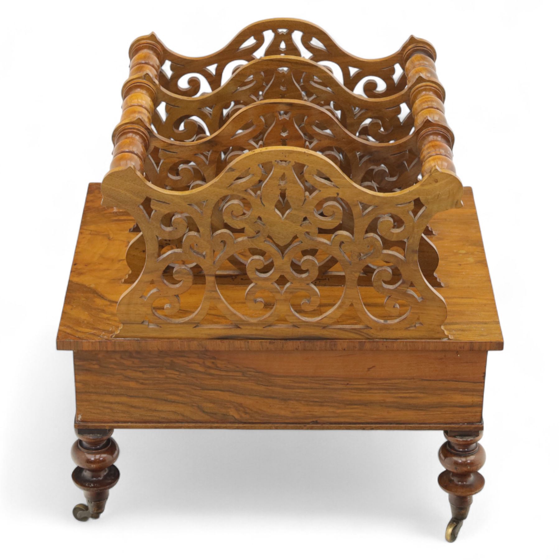 Victorian walnut Canterbury, scroll pierced divisions with turned carrying handles above a frieze drawer with knob handles, raised on turned legs terminating in brass castors