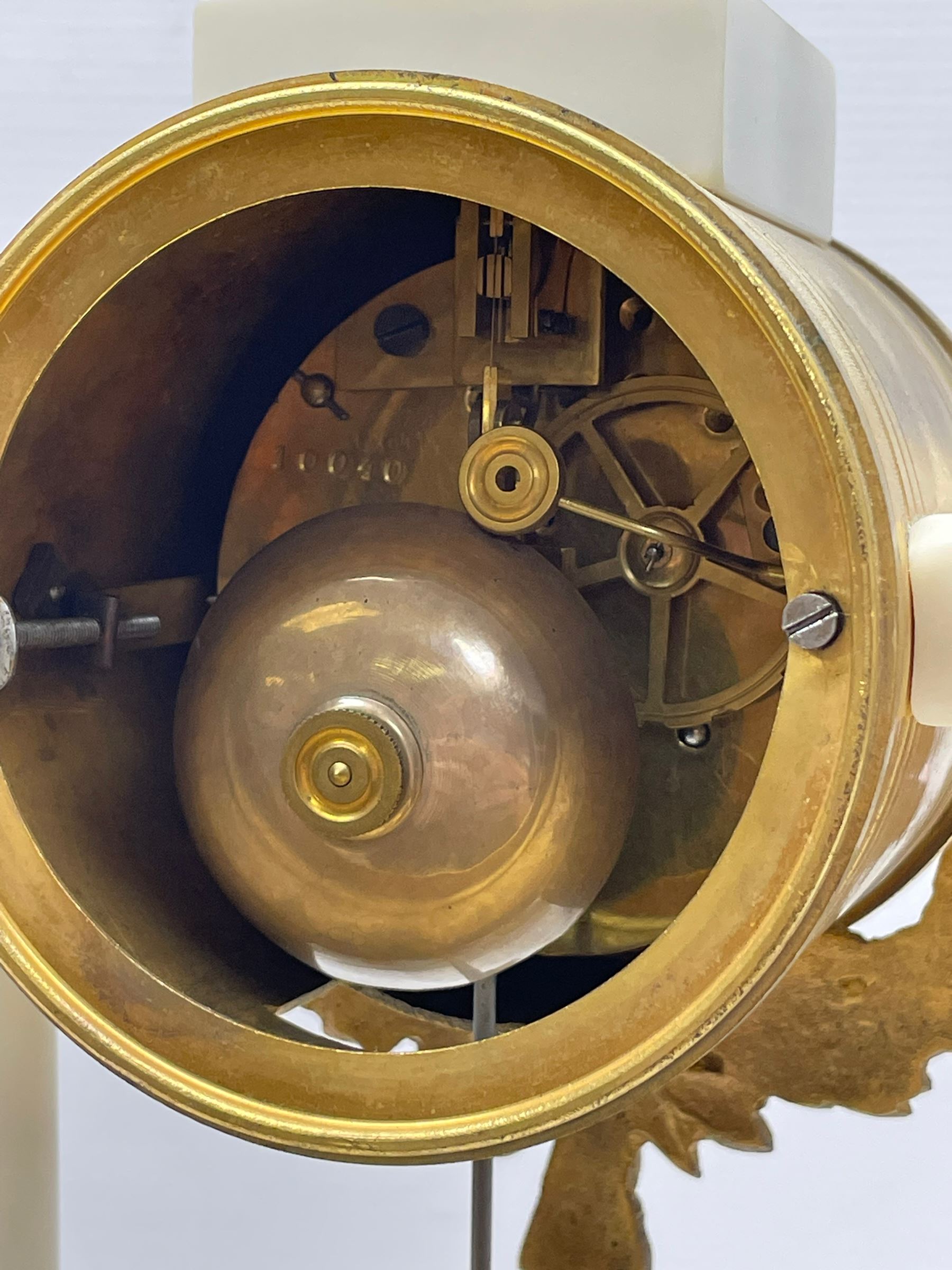 French - Late 19th century 8-day white marble and gilt metal portico clock garniture, the clock surmounted by an urn and raised on a pair of cylindrical pillars above a rectangular plinth base, white enamel dial with Arabic numerals and floral garlands, twin train countwheel striking movement, striking the hours and half hours on a bell, with a sunburst pendulum and gilt Louis XVI hands, garniture with matching twin light candelabra. With Key.   Candelabra H 30cm.