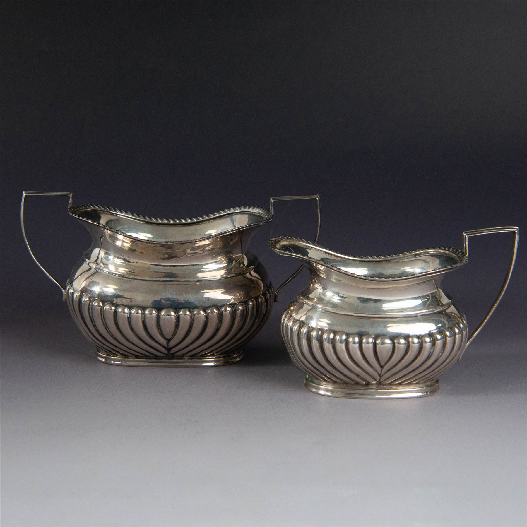 Victorian silver bachelors teapot, of part fluted oval form with ebonised wooden handle and finial, hallmarked Thomas Bradbury & Sons, London 1896, together with a Edwardian silver milk jug and open sucrier, of similar form with oblique gadrooned rims, hallmarked George Unite, Birmingham 1902 & 1906