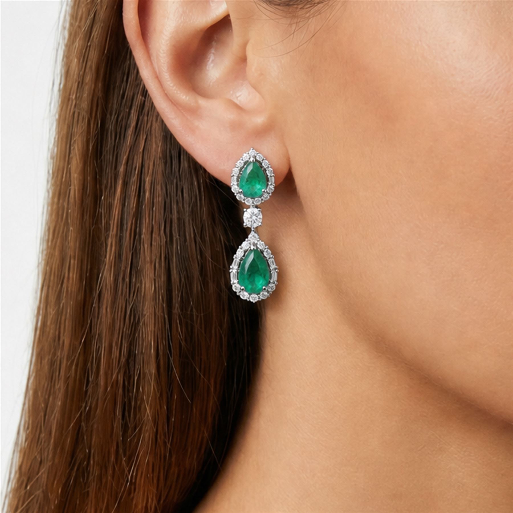 Pair of 18ct white gold emerald and diamond earrings, each stud set with two pear cut emeralds, surrounded by round brilliant cut and baguette cut diamonds, spaced by a single diamond, stamped, total emerald weight approx 4.15 carat, total diamond weight approx 1.50 carat